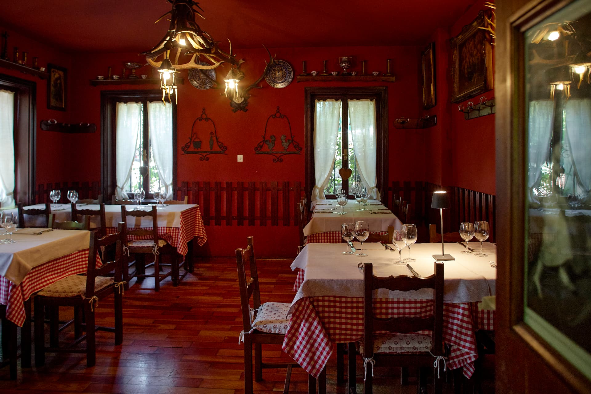Sala rossa con tovaglie a quadretti e lampadario in corna di cervo