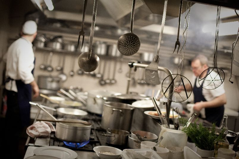 Cuochi al lavoro in cucina tra pentole di rame e mestoli appesi